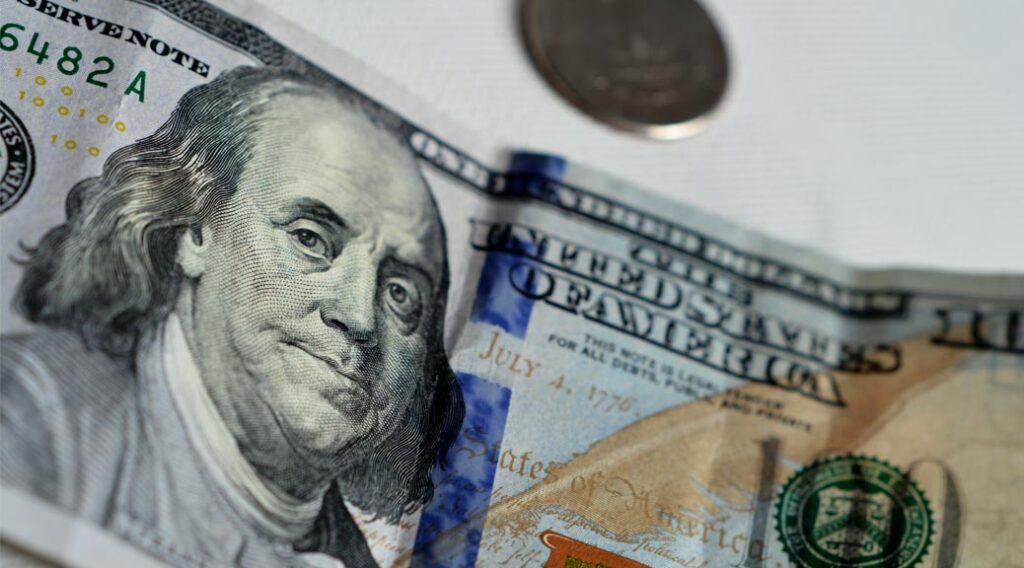 Close-up of a $100 bill with a coin in the background